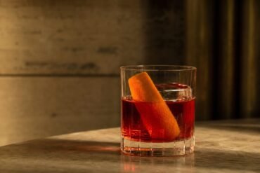 A ruby-red Negroni cocktail with clear ice and a wide orange peel in a rocks glass.