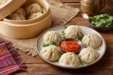 Steamed Nepalese momo dumplings with tomato achar and cilantro in a bamboo steamer.