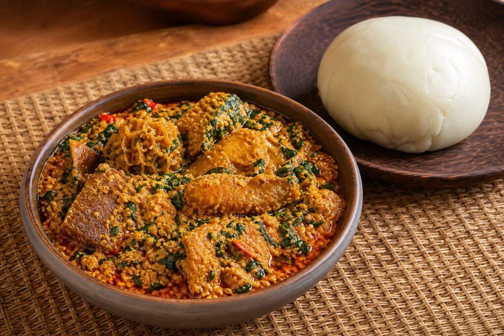 A bowl of Nigerian egusi soup with beef, leafy greens, red palm oil, and pounded yam.