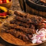 Smoky Nigerian suya beef skewers coated in spicy peanut seasoning with onions and tomatoes.
