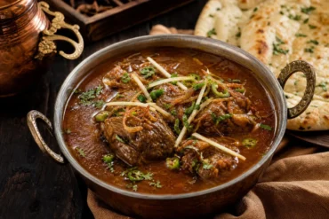 A bowl of Pakistani nihari beef stew with ginger, cilantro, green chili, and naan.