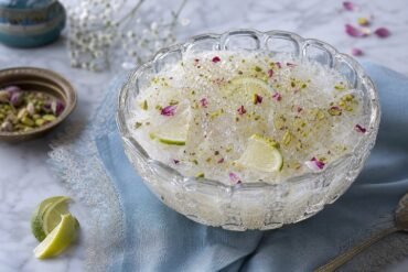 A chilled bowl of Persian faloodeh with rosewater noodles, lime, pistachios, and rose petals.