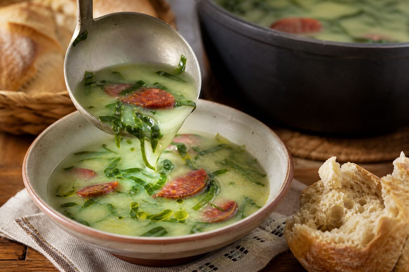 Portuguese caldo verde being ladled into a bowl with kale ribbons and chouriço.