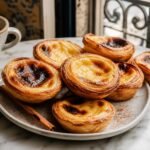 Portuguese pastel de nata custard tarts with flaky pastry, blistered tops, and cinnamon on a cafe table.