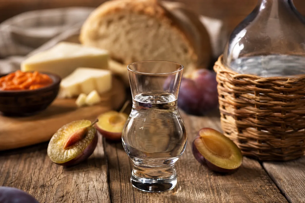 A close-up serving of Serbian plum rakija with plum slices, bread, cheese, and ajvar.