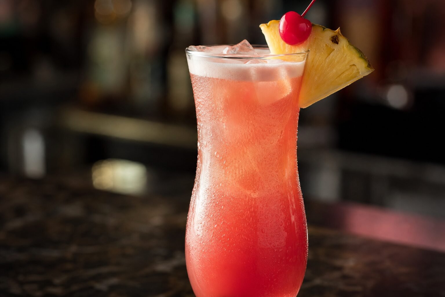 Close view of a chilled Singapore Sling with condensation, pineapple garnish, and cherry.