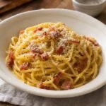Fresh homemade spaghetti alla carbonara with silky Pecorino sauce, crisp guanciale, black pepper, and grated cheese.
