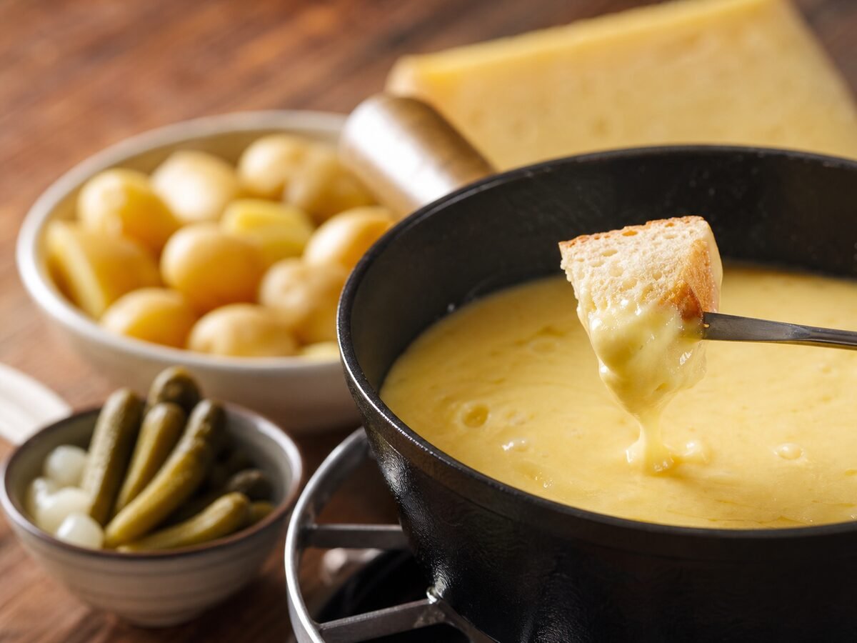 A close-up piece of crusty bread coated in melted Swiss cheese beside the fondue pot.