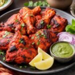 Charred red-orange Indian tandoori chicken with lemon, onion, cilantro, and mint chutney.