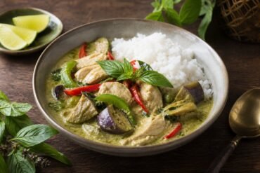 A bowl of Thai green curry with tender chicken, eggplant, red pepper, Thai basil, and jasmine rice.