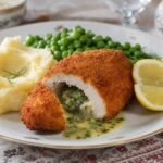 Golden breadcrumb-coated Ukrainian chicken Kiev sliced open with herb butter, mashed potatoes, peas, and lemon.