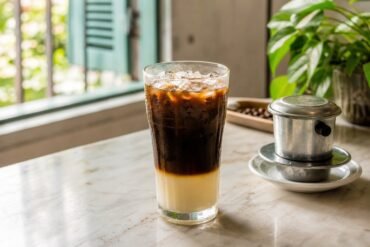 Vietnamese iced coffee layered with dark coffee and sweetened condensed milk in a clear glass with a phin filter.