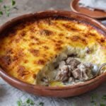 Golden Albanian tave kosi casserole with tender lamb and creamy yogurt topping in an earthenware dish.