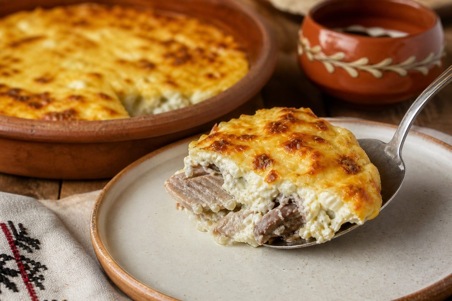 A spoonful of Albanian tave kosi showing tender lamb beneath its browned yogurt topping.