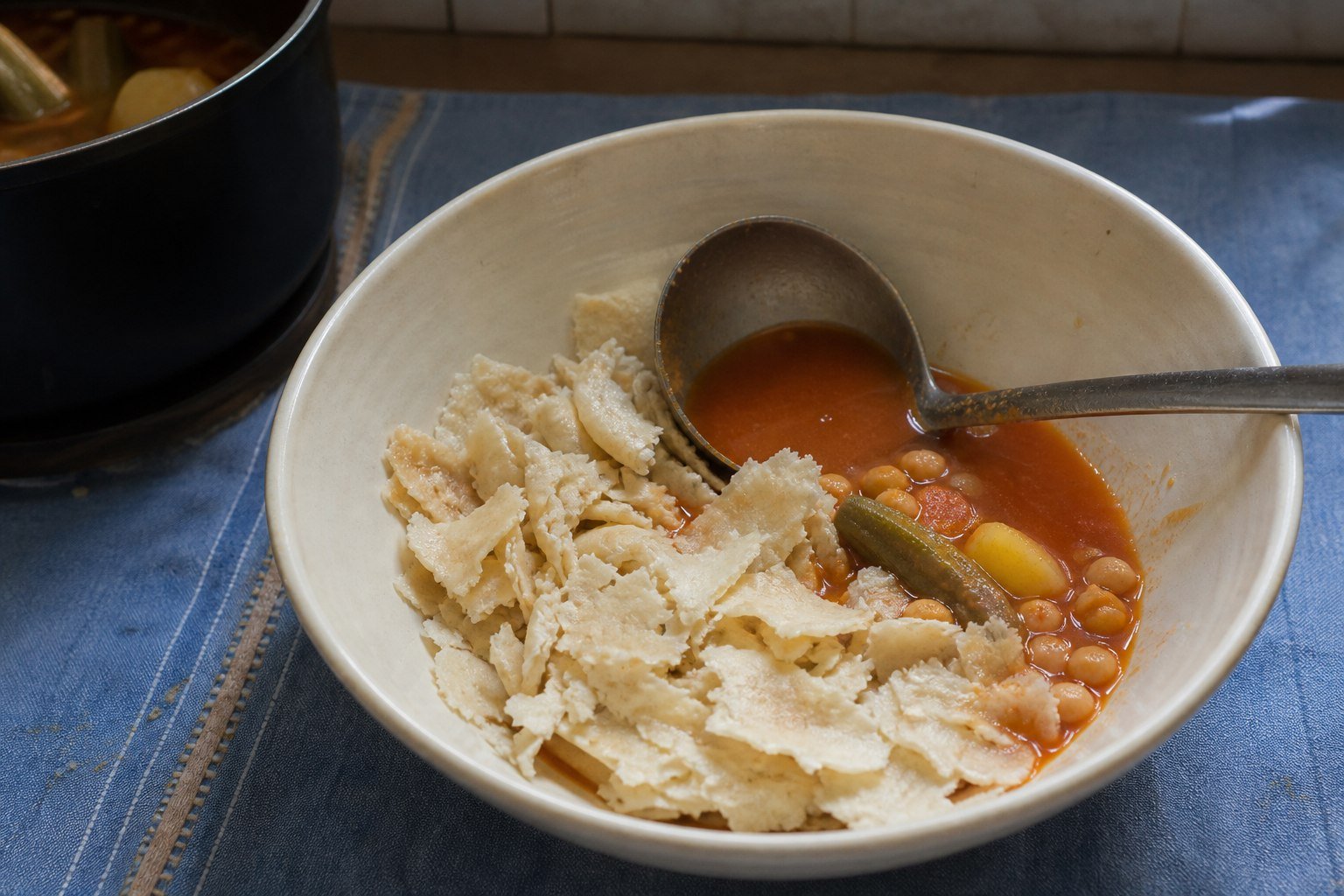 Torn rougag flatbread being moistened with chickpea and vegetable broth for chakhchoukha.