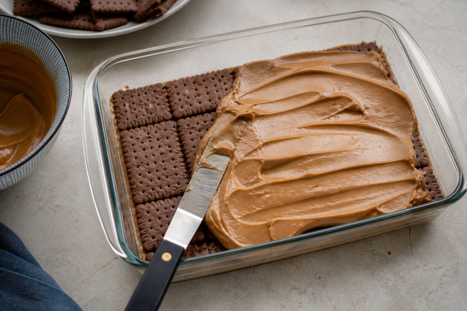 Argentine chocotorta being layered with chocolate biscuits and dulce de leche cream.