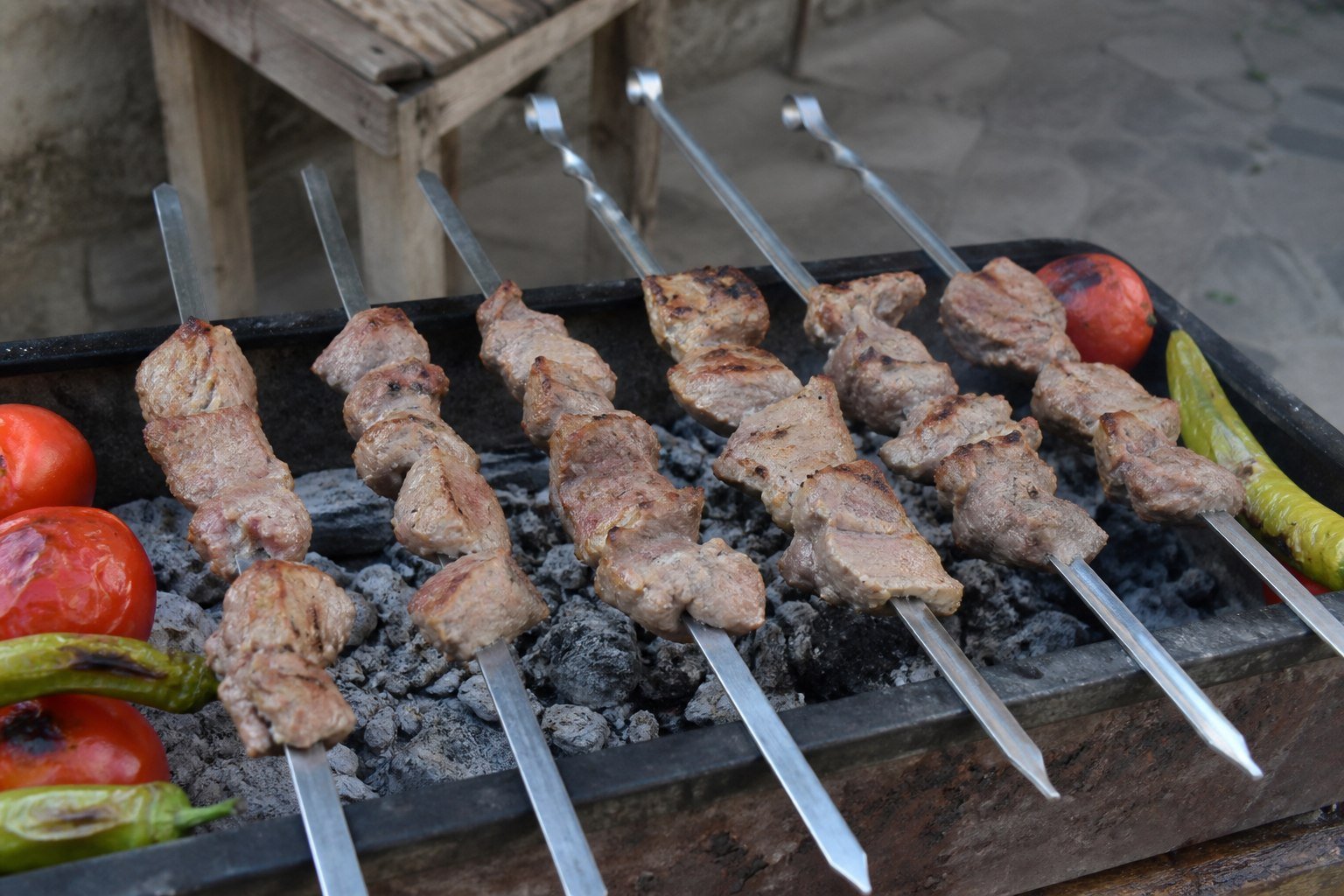 Pork shoulder and vegetables cooking on flat skewers over charcoal for Armenian khorovats.