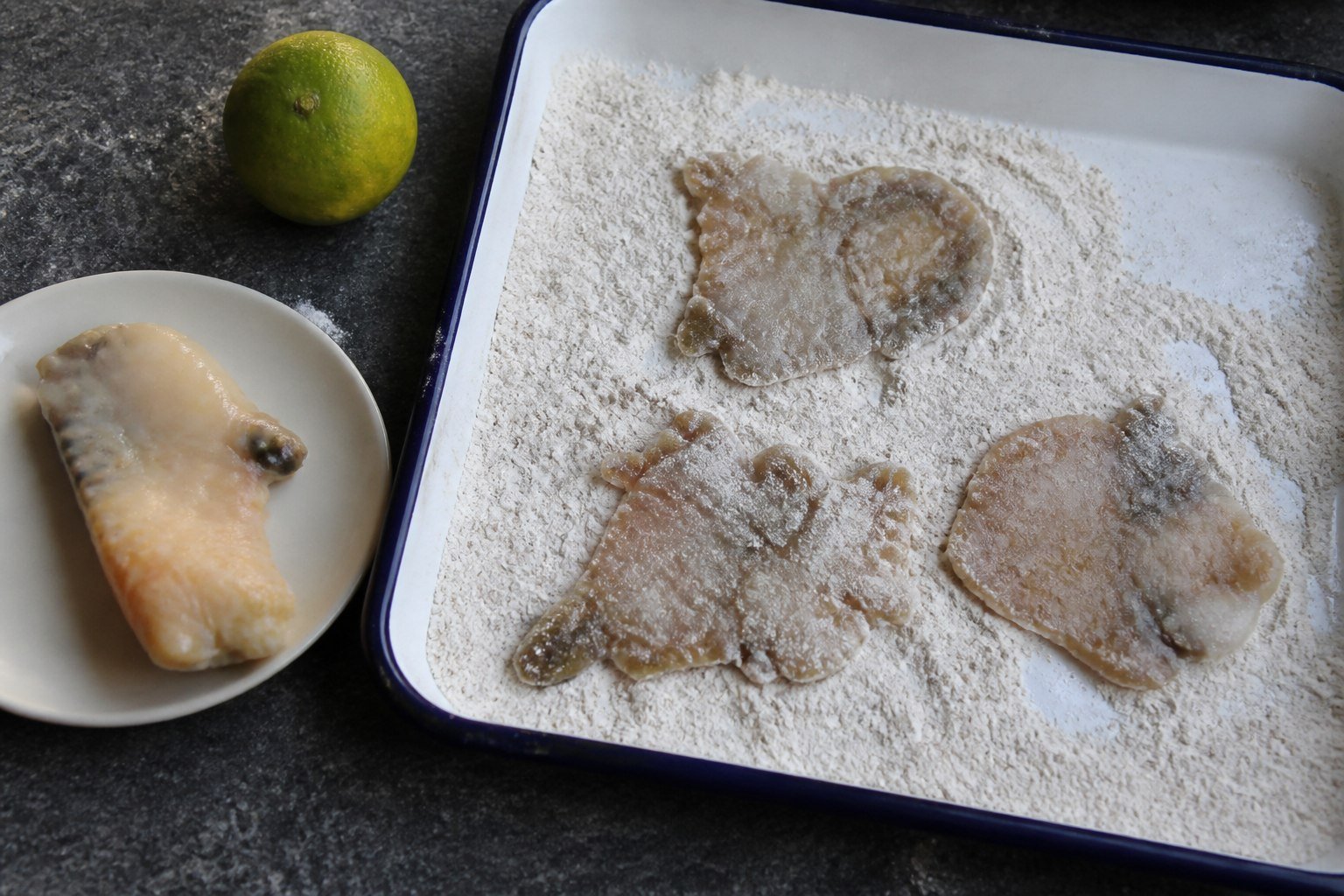 Pounded Bahamian conch pieces in seasoned flour beside intact cleaned conch meat and lime.