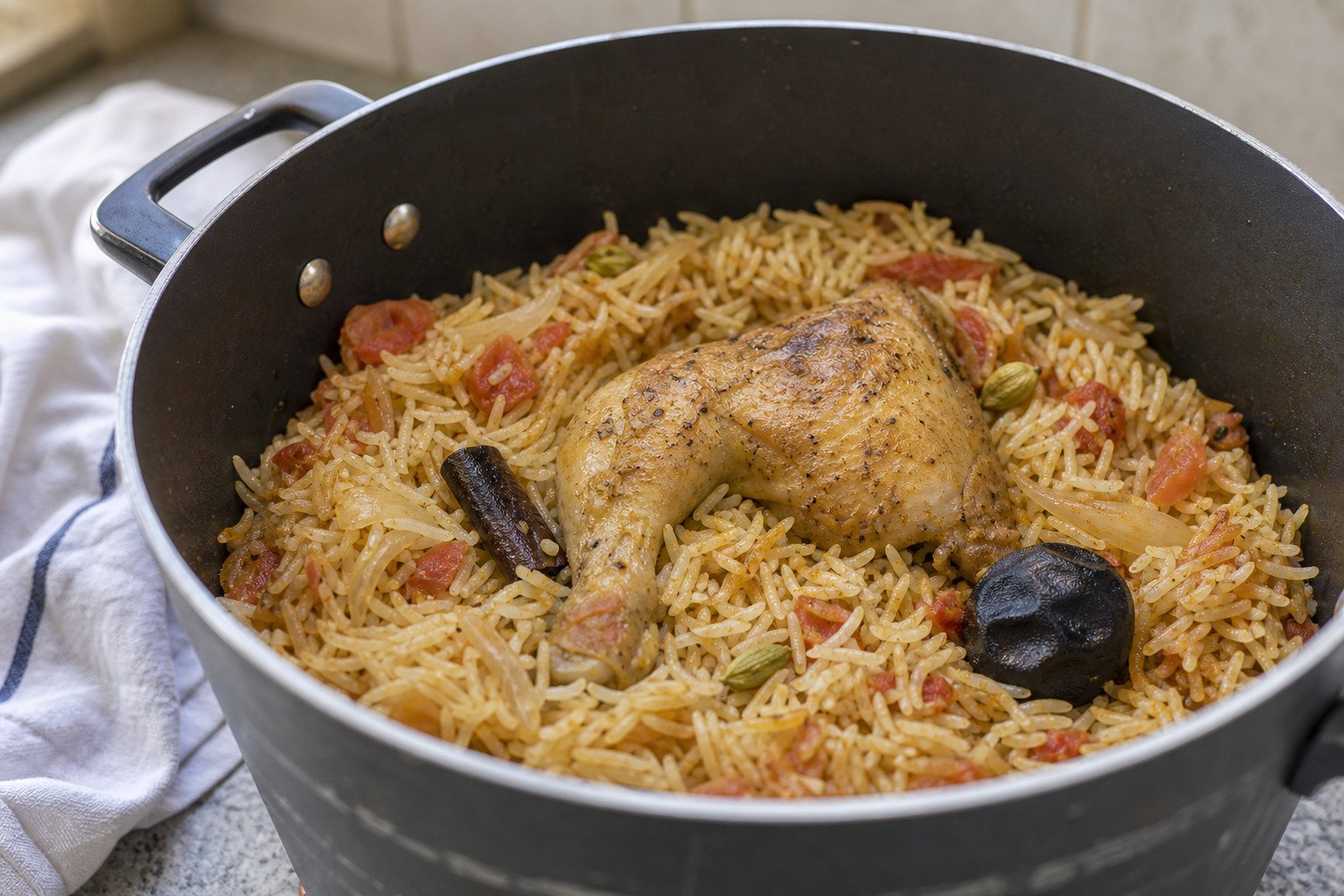 Bahraini chicken machboos cooking in a pot with rice, spices, and dried lime.