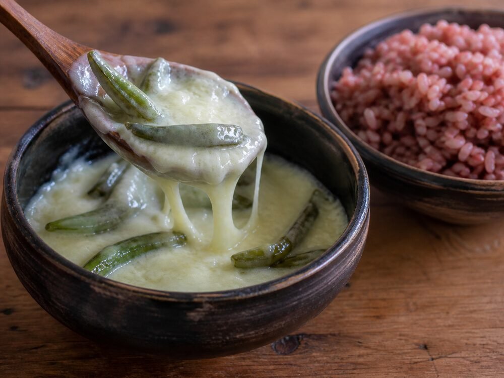Creamy ema datshi with green chilies being served beside red rice.
