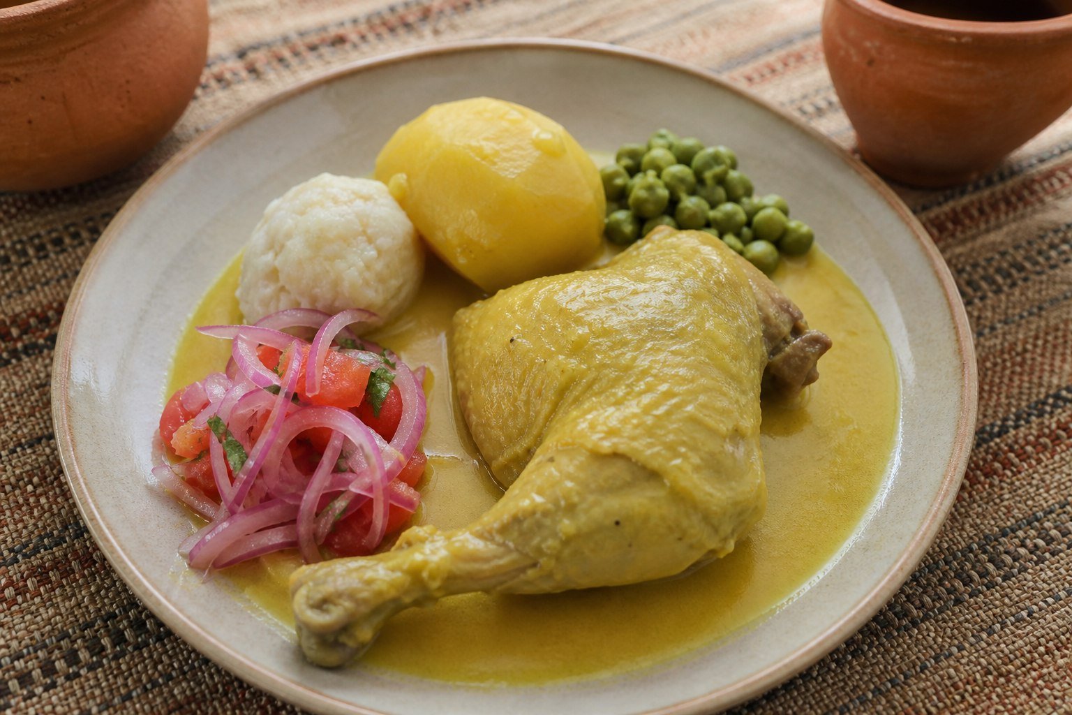 Bolivian sajta de pollo with yellow chile chicken, potato, tunta, peas, and onion-tomato sarza.