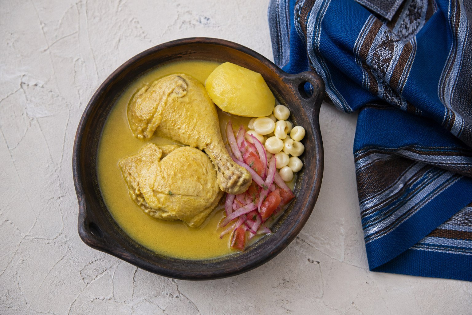 Bolivian yellow chile chicken served in a clay bowl with potato, white corn, and sarza.