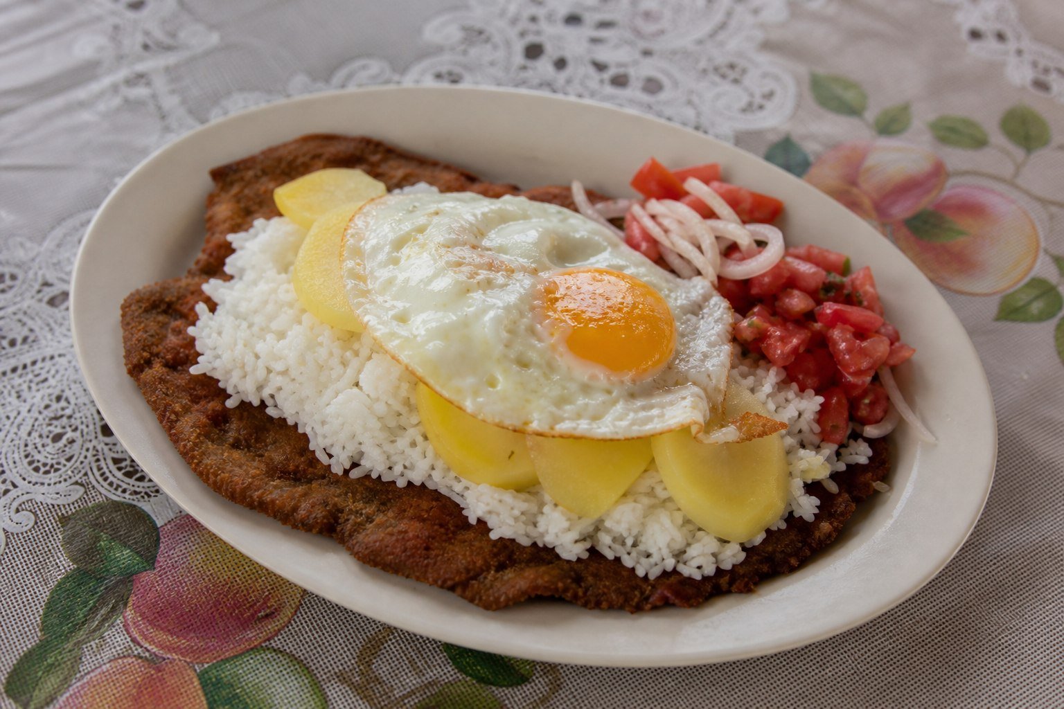Bolivian silpancho with breaded beef, rice, potatoes, fried egg, and tomato salad.