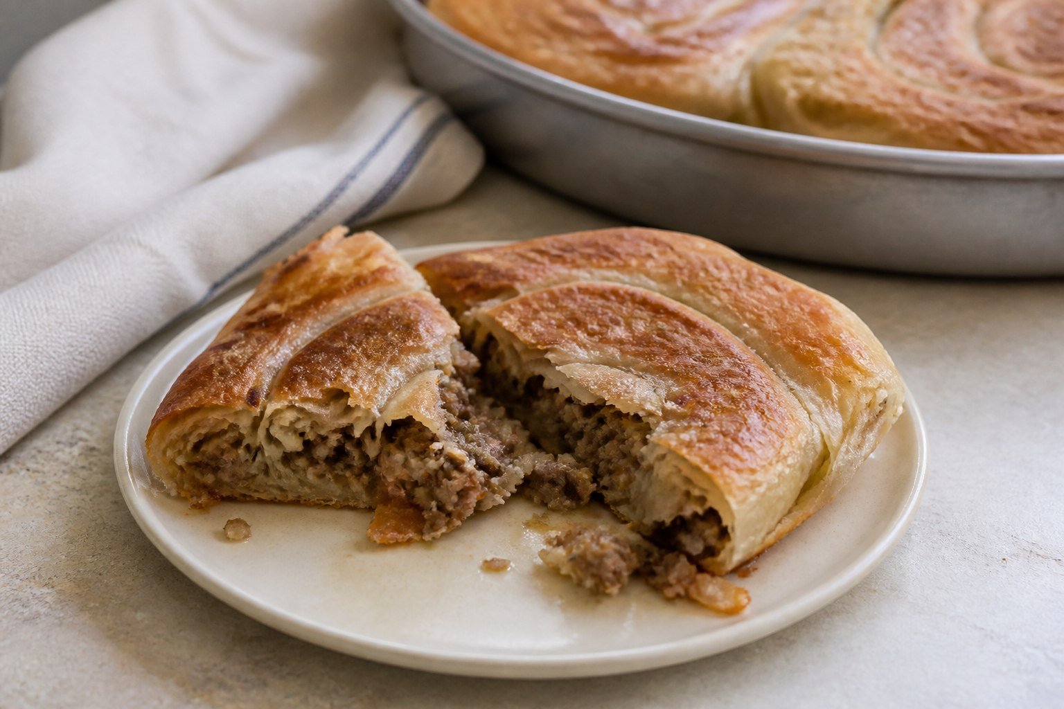 Cut wedges of Bosnian burek showing thin pastry and beef-onion filling.