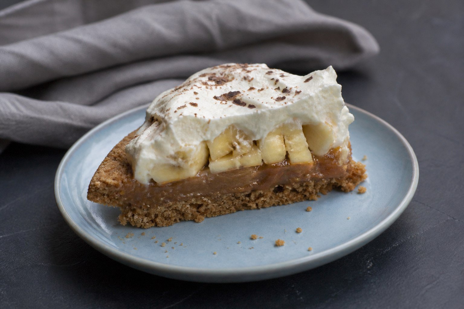 A slice of British banoffee pie showing crumb, caramel, banana, and cream layers.