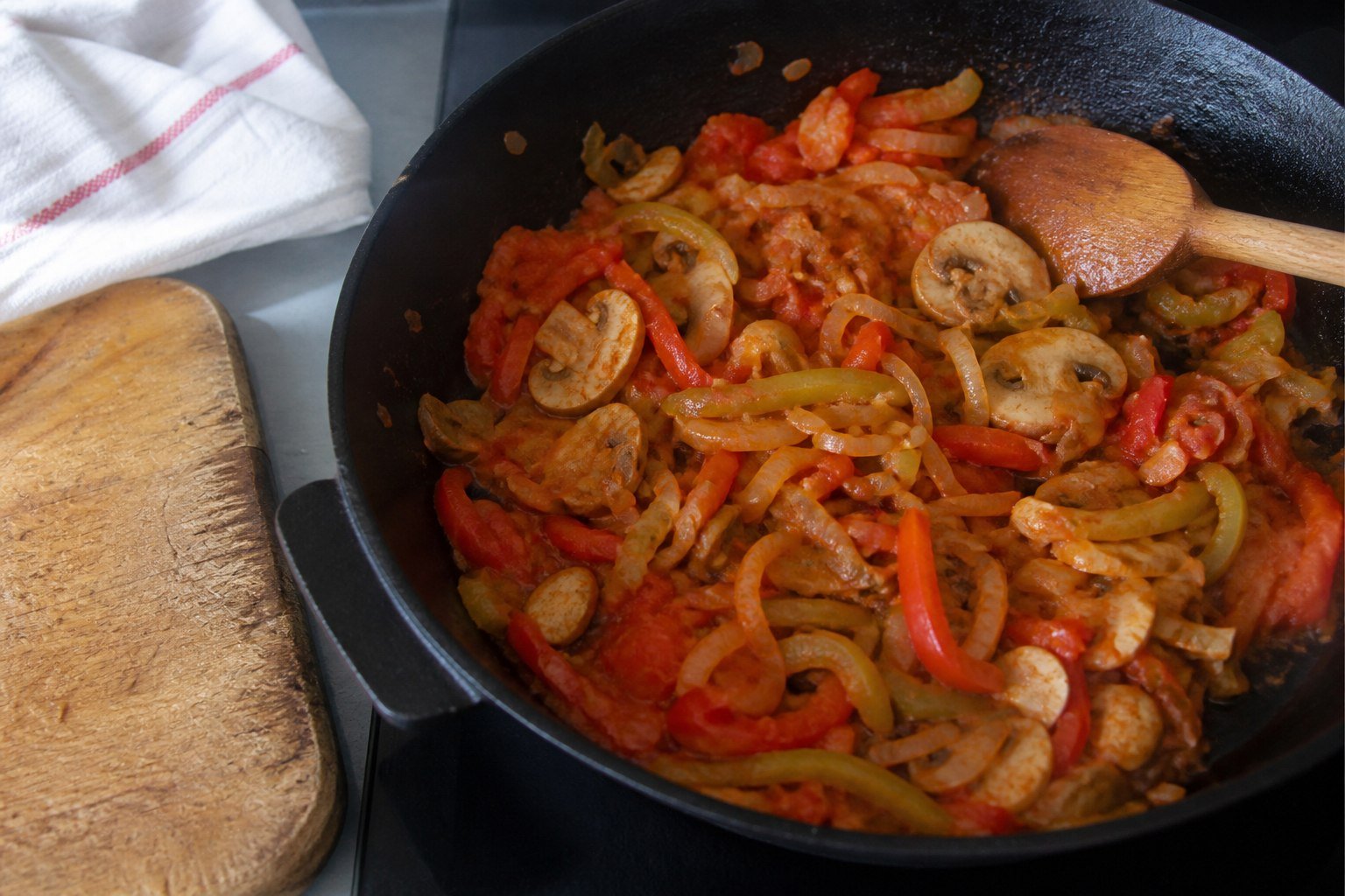 Onions, peppers, mushrooms, and tomato cooking in a skillet for Bulgarian kavarma.