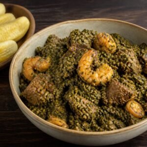 Cameroonian ndolé with beef and shrimp served beside boiled plantains.