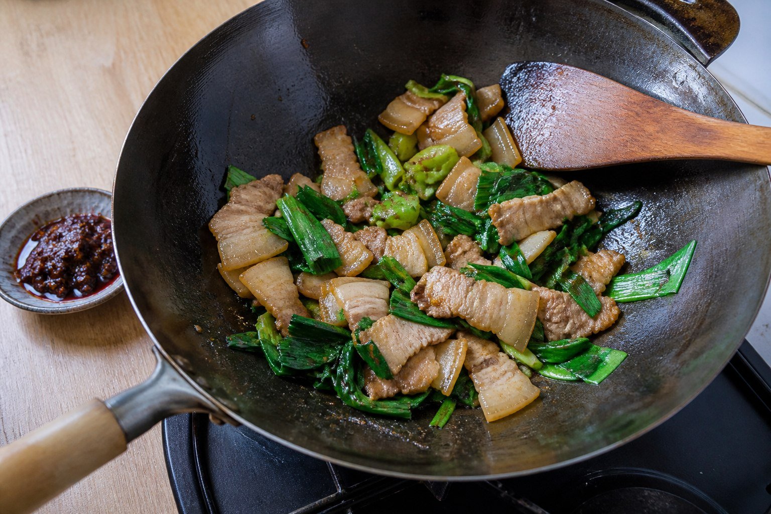 Pork belly and green garlic cooking in a carbon-steel wok.