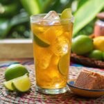 Chilled Colombian aguapanela with lime over ice, served with panela and fresh citrus on a colorful table.