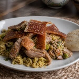 Colombian lechona Tolimense with seasoned rice, peas, roast pork, crisp skin, and arepa.