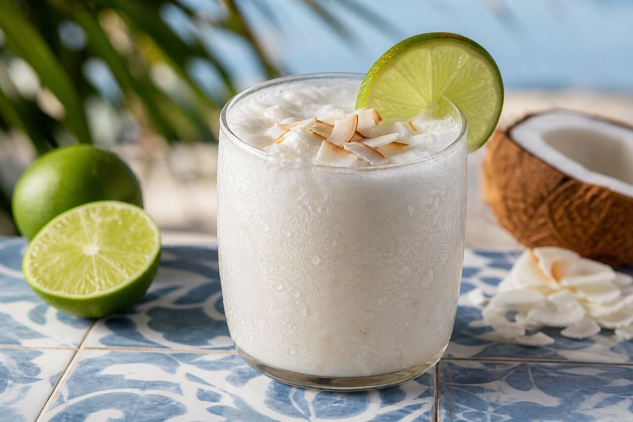 A close serving of creamy Colombian coconut limeade with condensation and a lime wedge.