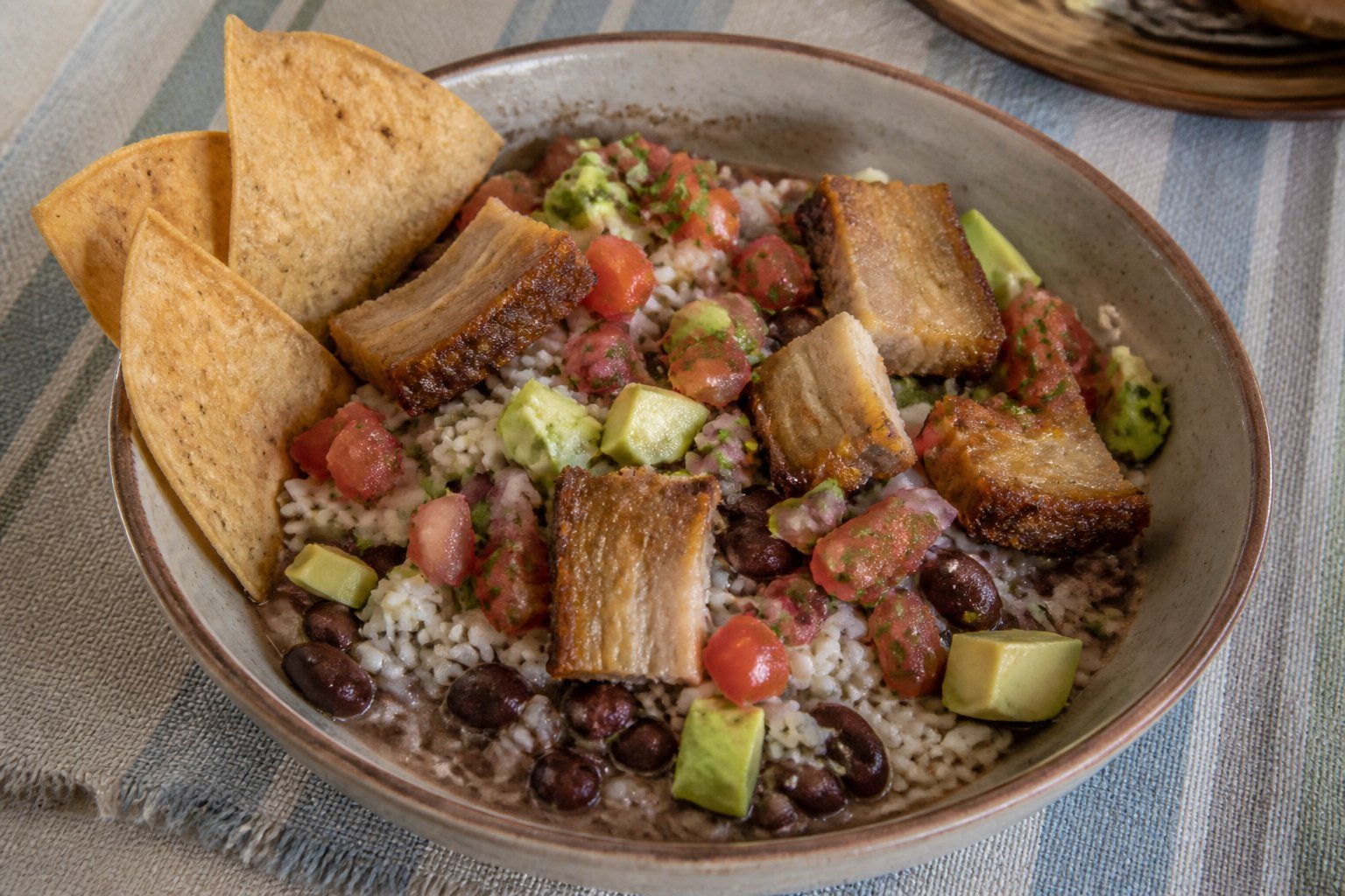 Costa Rican chifrijo with rice, red beans, pork-belly chicharron, pico de gallo, avocado, and chips.
