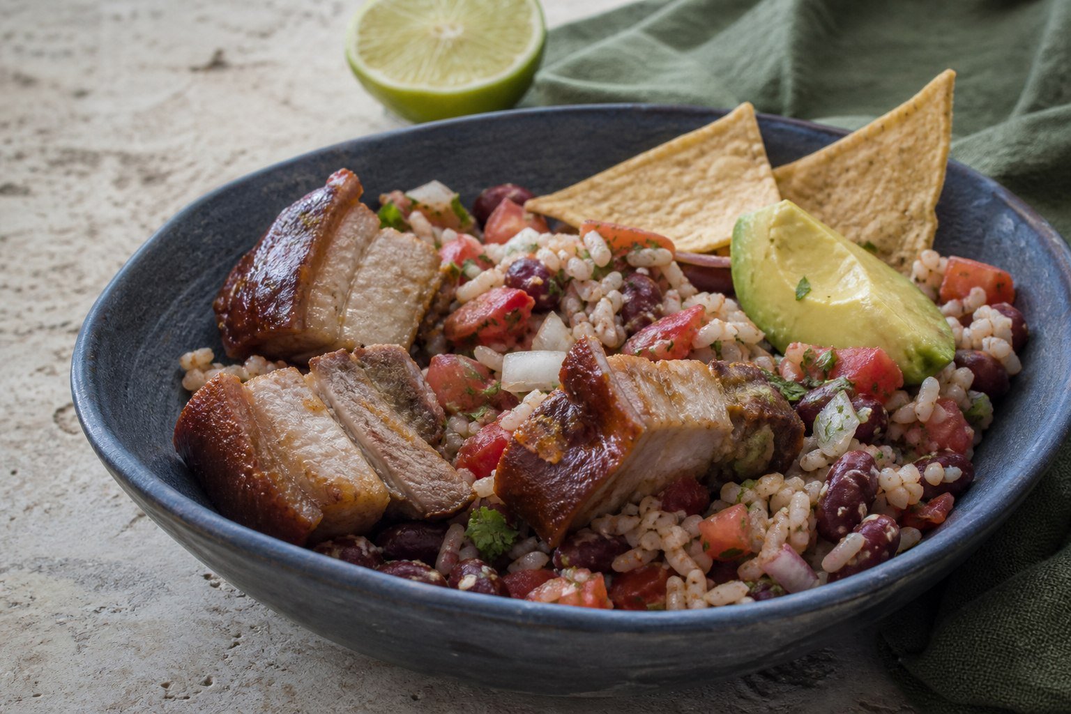 A close serving of chifrijo with mixed rice and beans, layered pork belly, salsa, avocado, and chips.