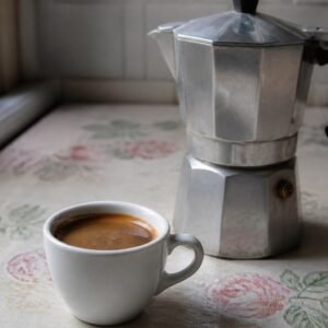 A small cup of Cuban cafe cubano beside a stovetop moka pot.