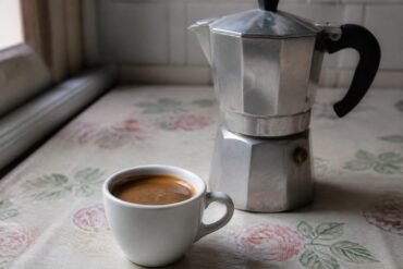 A small cup of Cuban cafe cubano beside a stovetop moka pot.