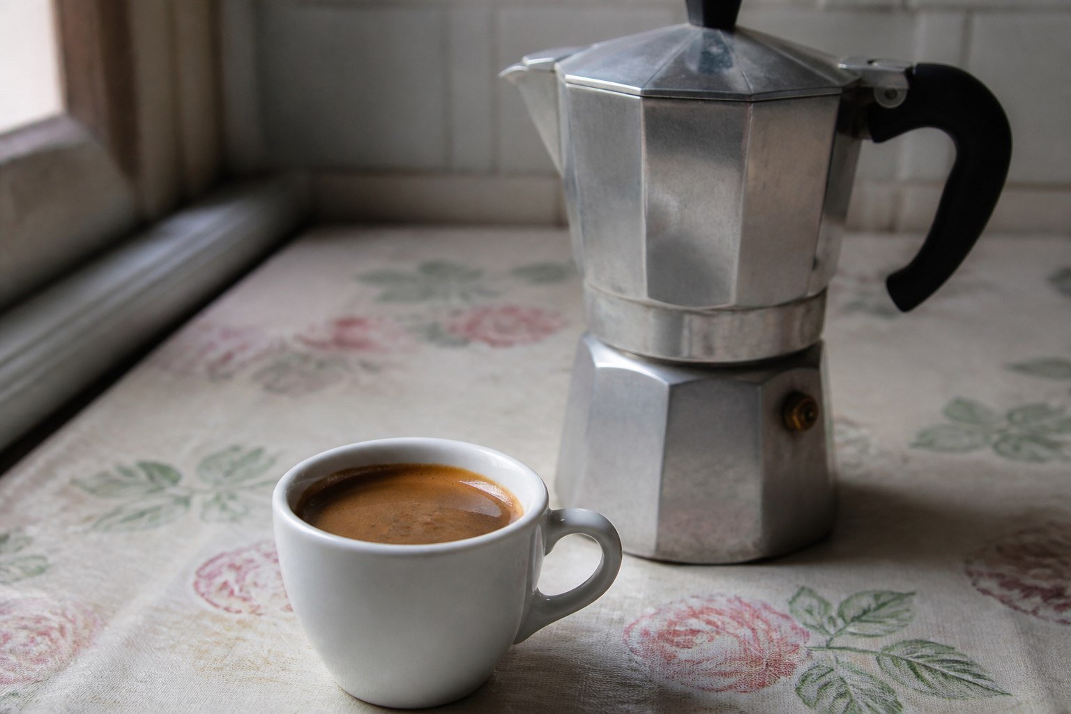 A small cup of Cuban cafe cubano beside a stovetop moka pot.