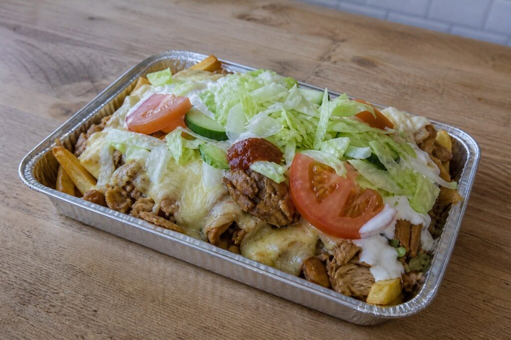 Dutch kapsalon layered with fries, chicken, Gouda, salad, garlic sauce, and sambal.