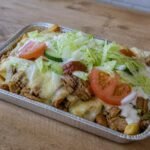 Dutch kapsalon layered with fries, chicken, Gouda, salad, garlic sauce, and sambal.