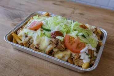 Dutch kapsalon layered with fries, chicken, Gouda, salad, garlic sauce, and sambal.