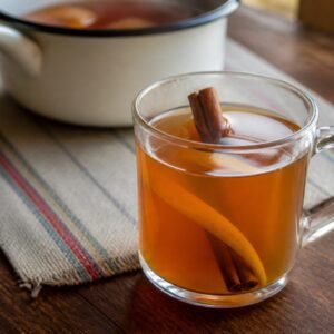 Warm Ecuadorian canelazo with cinnamon and orange in a clear heatproof mug.