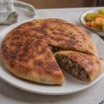 Egyptian hawawshi flatbread filled with seasoned beef and served with pickles.
