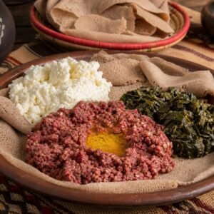 Ethiopian kitfo with ayib, collard greens, and injera on a rustic platter.