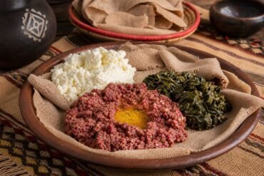 Ethiopian kitfo with ayib, collard greens, and injera on a rustic platter.