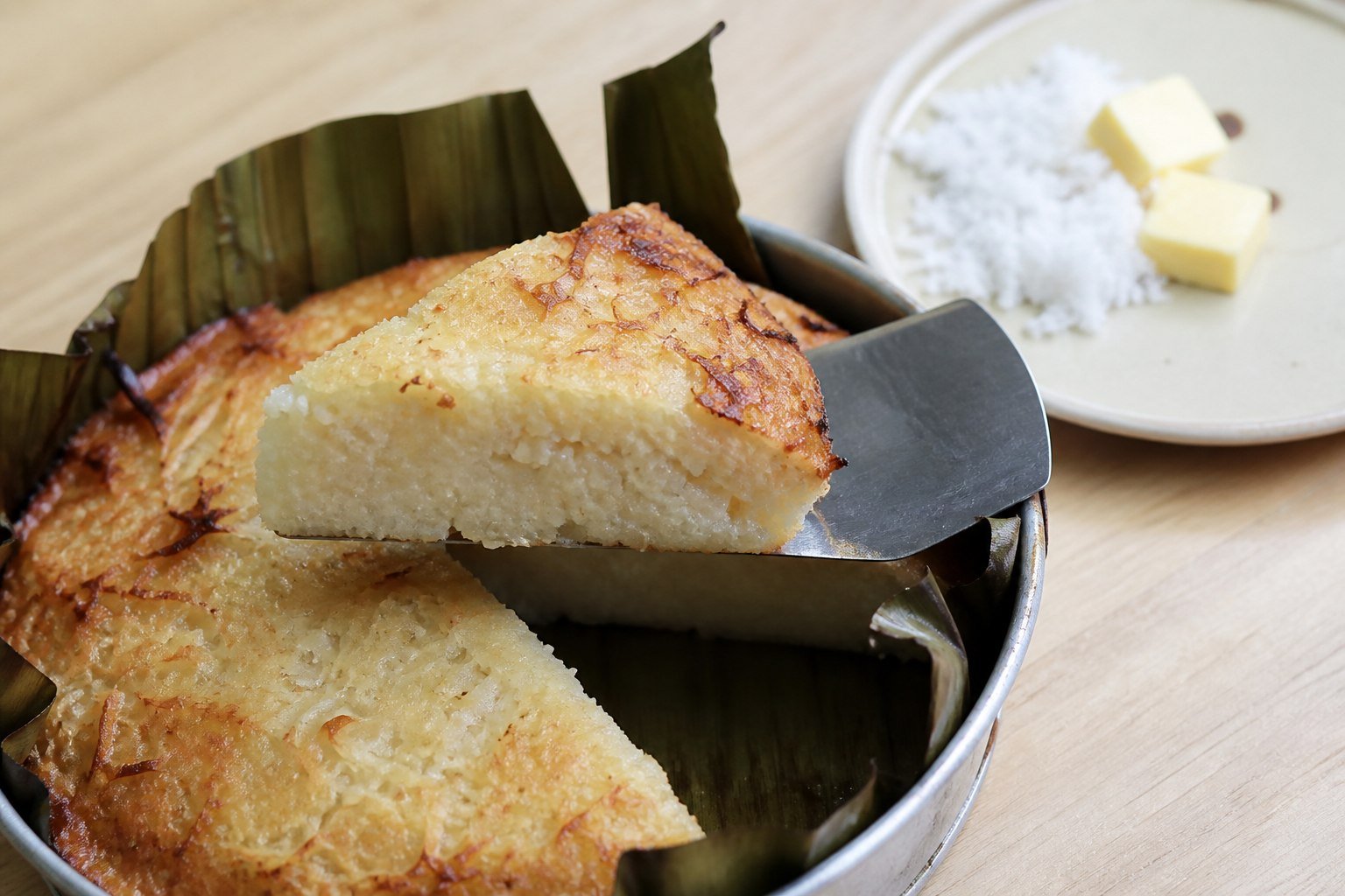 A warm wedge of Filipino bibingka lifted from a banana-leaf-lined pan, showing its dense rice-cake crumb.
