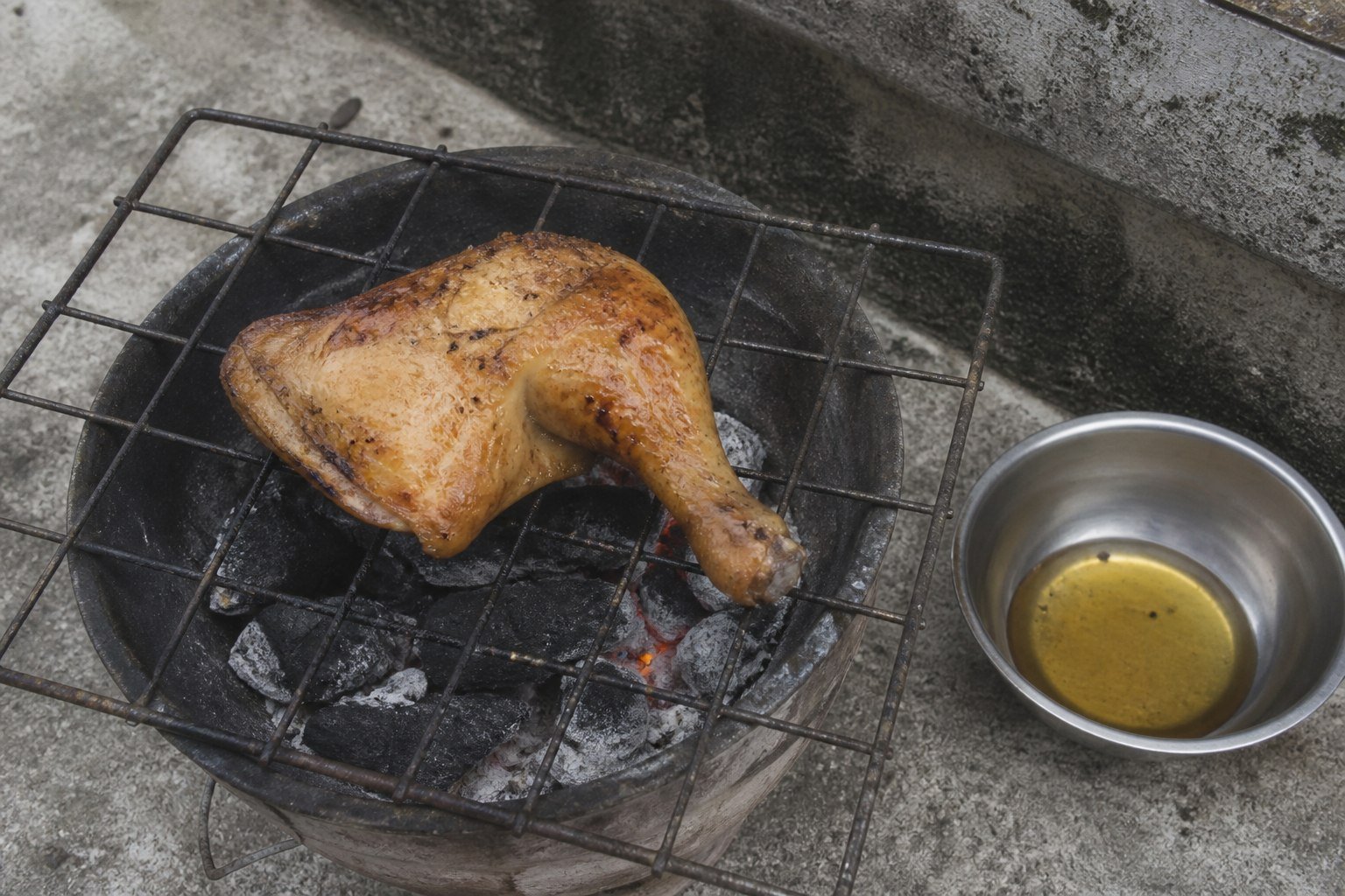 A single Filipino chicken inasal leg quarter grilling over charcoal.