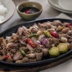 Filipino pork sisig with onions, chilies, and calamansi on a sizzling platter.